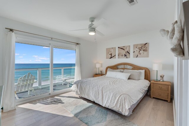 bedroom with light wood-type flooring, a water view, ceiling fan, and access to exterior