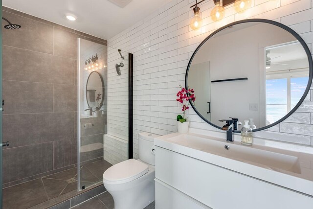 bathroom with tile walls, vanity, tile patterned flooring, a shower with door, and toilet