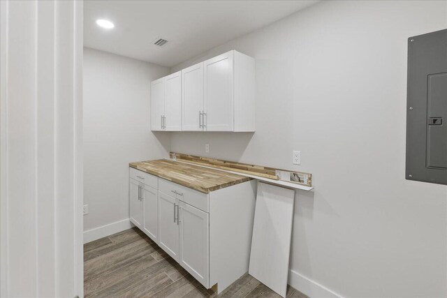 kitchen with electric panel, white cabinetry, wood-type flooring, and wood counters