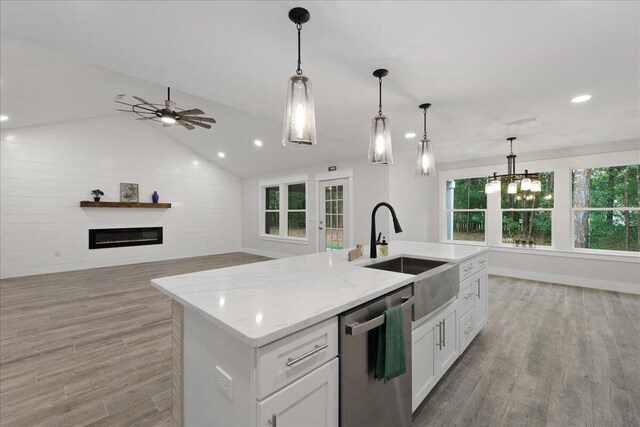 kitchen featuring vaulted ceiling, stainless steel dishwasher, a wealth of natural light, and an island with sink