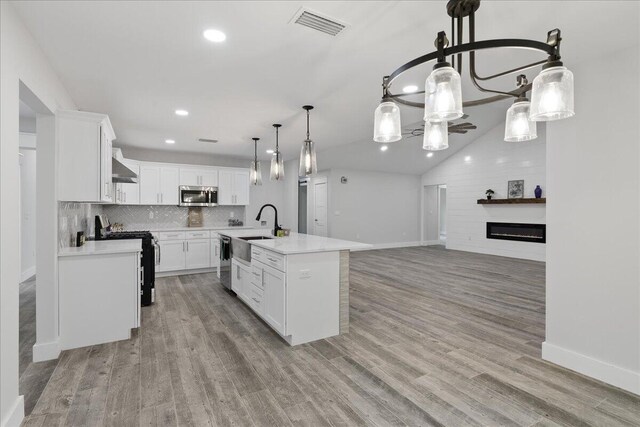 kitchen with pendant lighting, a kitchen island with sink, appliances with stainless steel finishes, light hardwood / wood-style floors, and white cabinetry