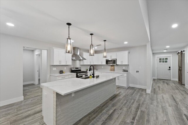 kitchen with appliances with stainless steel finishes, a barn door, white cabinetry, and wall chimney exhaust hood