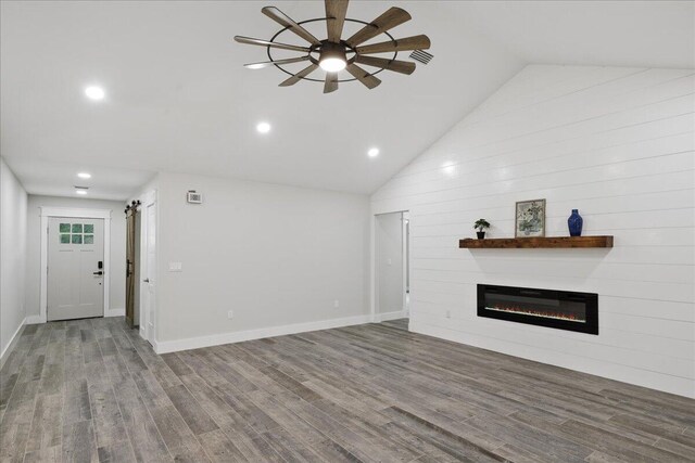 unfurnished living room featuring a barn door, ceiling fan, wood-type flooring, and vaulted ceiling