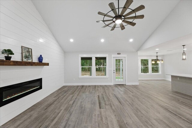 unfurnished living room with ceiling fan with notable chandelier, high vaulted ceiling, and light hardwood / wood-style flooring