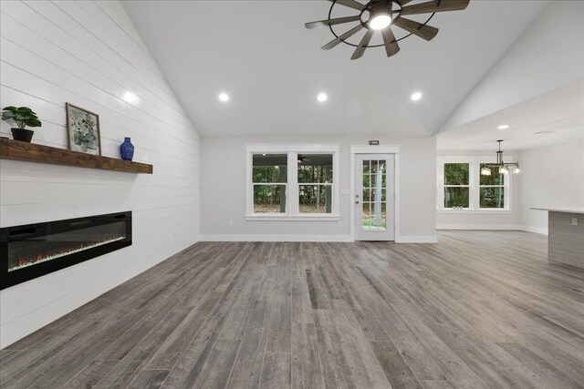 unfurnished living room with plenty of natural light, high vaulted ceiling, wood-type flooring, and ceiling fan with notable chandelier