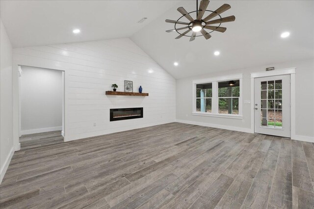 unfurnished living room featuring light hardwood / wood-style flooring, vaulted ceiling, ceiling fan, and wood walls