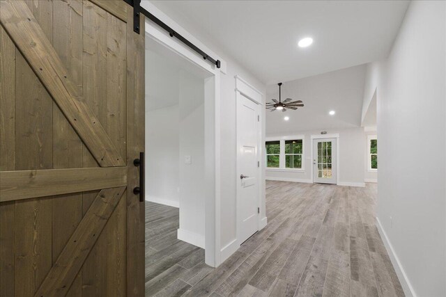 hall with a barn door, hardwood / wood-style floors, and lofted ceiling