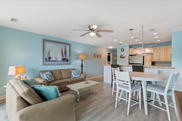 living room with ceiling fan with notable chandelier and light hardwood / wood-style flooring