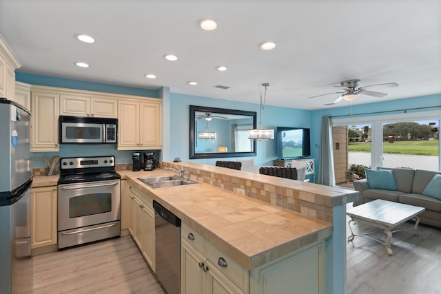 kitchen featuring light hardwood / wood-style floors, sink, kitchen peninsula, appliances with stainless steel finishes, and hanging light fixtures