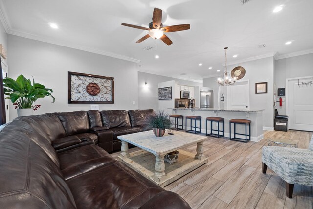 living room featuring light wood-type flooring, ceiling fan with notable chandelier, crown molding, and sink