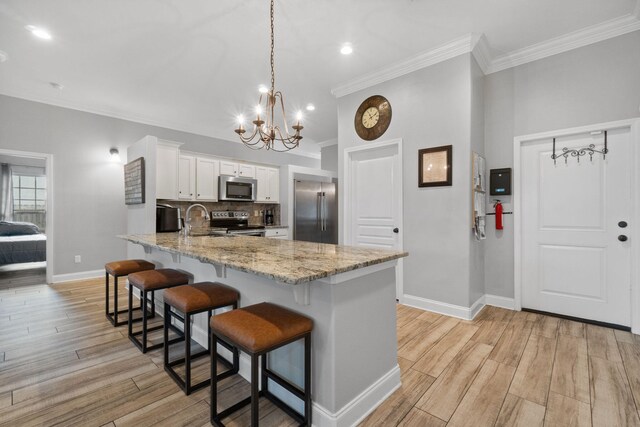 kitchen with a kitchen breakfast bar, light hardwood / wood-style flooring, stainless steel appliances, ornamental molding, and white cabinets