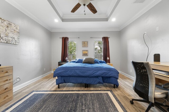 bedroom with light hardwood / wood-style flooring, ceiling fan, ornamental molding, and a tray ceiling