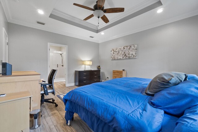 bedroom featuring a raised ceiling, light hardwood / wood-style floors, crown molding, ensuite bath, and ceiling fan