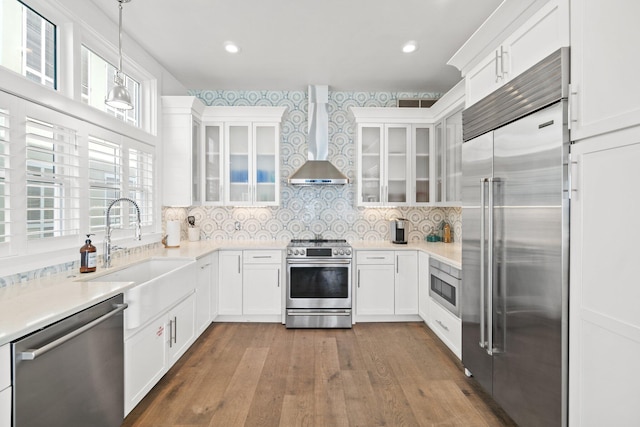 kitchen featuring decorative light fixtures, wall chimney exhaust hood, wood-type flooring, appliances with stainless steel finishes, and white cabinets