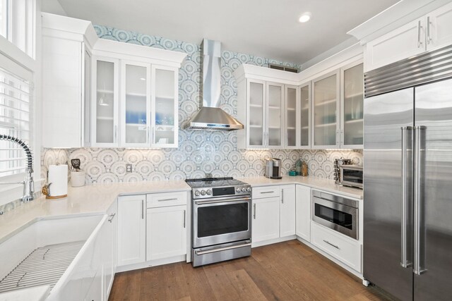 kitchen featuring white cabinets, sink, wall chimney range hood, dark hardwood / wood-style floors, and built in appliances