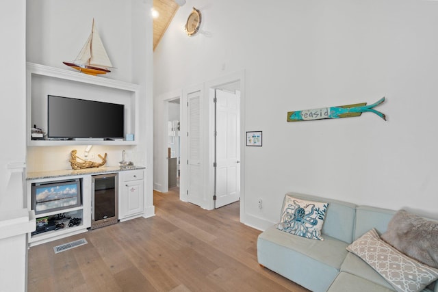 living room featuring beverage cooler, high vaulted ceiling, light hardwood / wood-style floors, and indoor bar