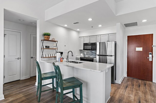 kitchen with black appliances, kitchen peninsula, a kitchen bar, and dark hardwood / wood-style floors