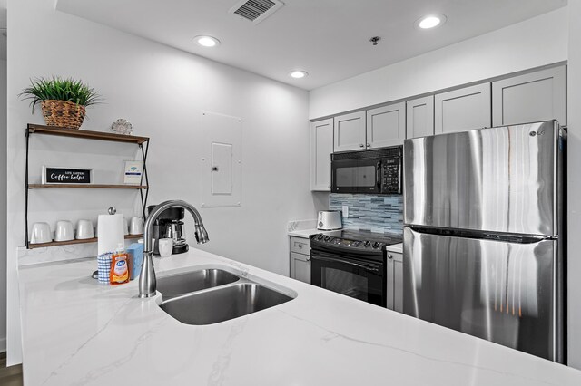 kitchen featuring decorative backsplash, light stone countertops, gray cabinets, black appliances, and sink