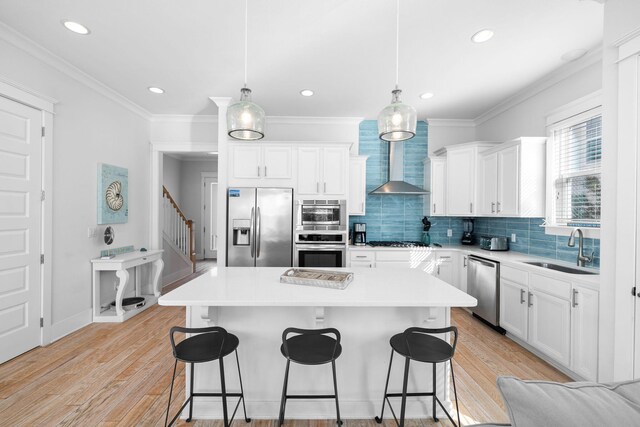 kitchen with pendant lighting, sink, wall chimney range hood, a kitchen island, and stainless steel appliances