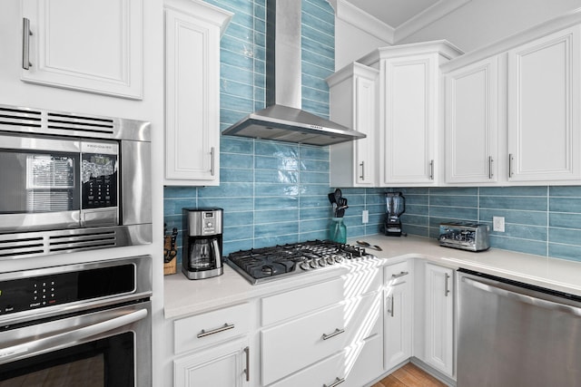 kitchen with white cabinets, ornamental molding, wall chimney exhaust hood, backsplash, and appliances with stainless steel finishes