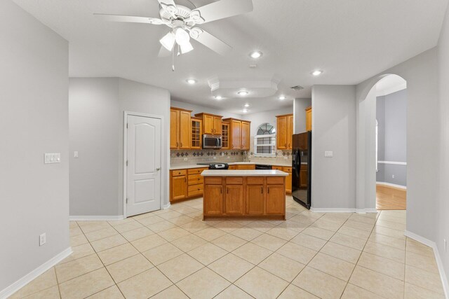 kitchen featuring light tile patterned floors, black fridge, ceiling fan, a kitchen island, and decorative backsplash