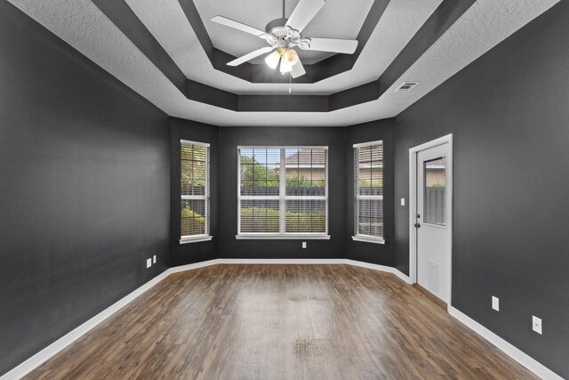 unfurnished room featuring a tray ceiling, ceiling fan, dark hardwood / wood-style flooring, and a textured ceiling