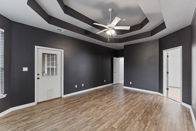 spare room with a raised ceiling, a textured ceiling, hardwood / wood-style floors, and ceiling fan