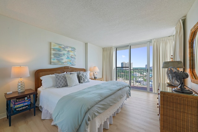 bedroom with a textured ceiling, access to exterior, light wood-type flooring, and floor to ceiling windows