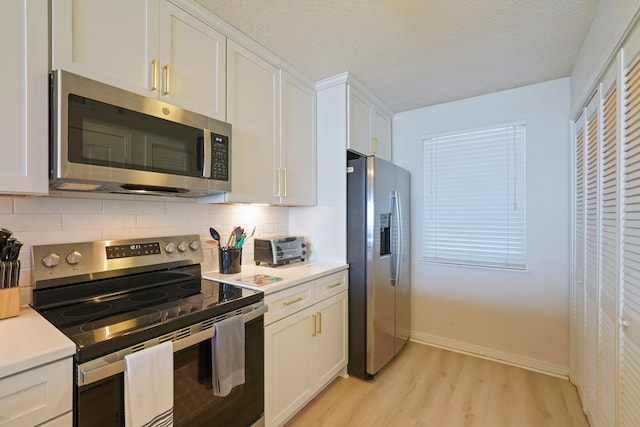 kitchen with backsplash, appliances with stainless steel finishes, white cabinets, and light hardwood / wood-style floors