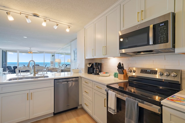 kitchen featuring backsplash, appliances with stainless steel finishes, a textured ceiling, white cabinetry, and sink