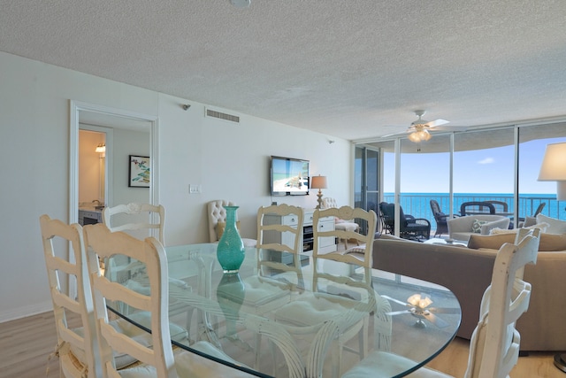 dining area with light hardwood / wood-style floors, a textured ceiling, a wall of windows, and ceiling fan