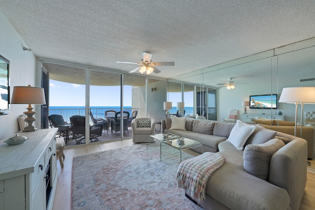 living room with a water view, expansive windows, a textured ceiling, light hardwood / wood-style floors, and ceiling fan