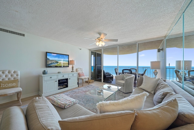 living room featuring ceiling fan, a textured ceiling, a wall of windows, and hardwood / wood-style floors