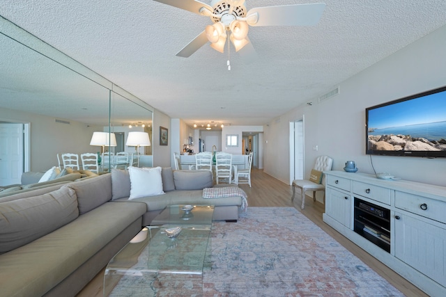 living room with a textured ceiling, light wood-type flooring, and ceiling fan