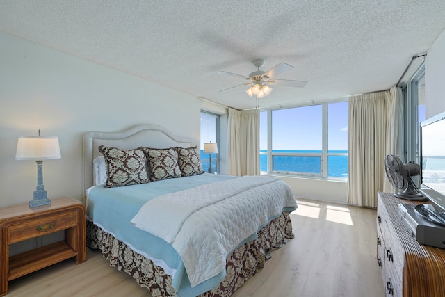 bedroom featuring light hardwood / wood-style flooring, a textured ceiling, multiple windows, and ceiling fan