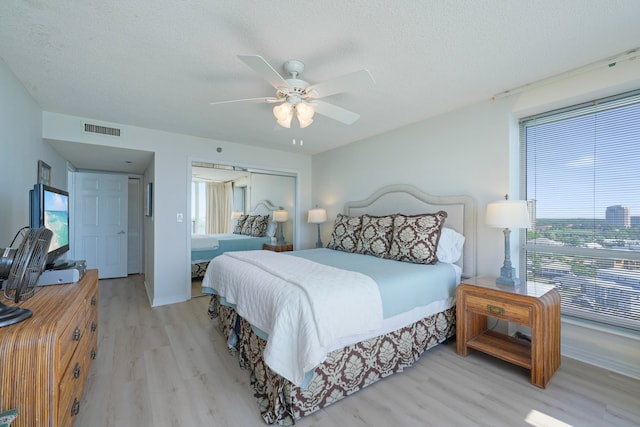 bedroom with a closet, a textured ceiling, light hardwood / wood-style floors, and ceiling fan