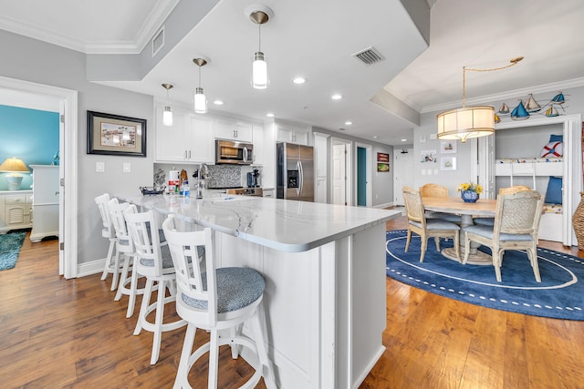 kitchen featuring pendant lighting, white cabinetry, kitchen peninsula, appliances with stainless steel finishes, and hardwood / wood-style flooring