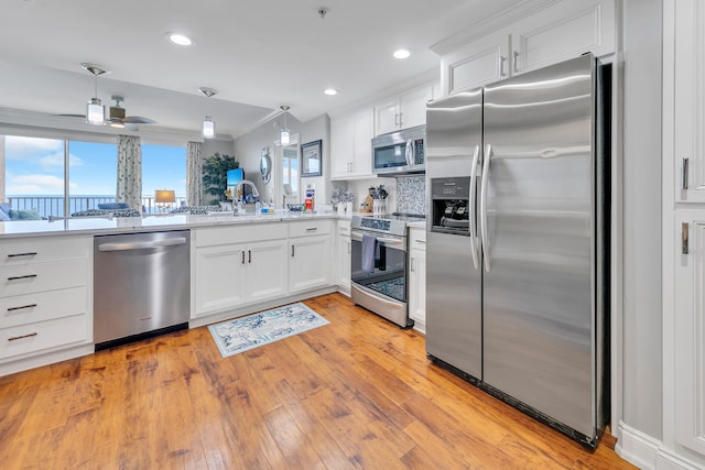 kitchen featuring light hardwood / wood-style floors, white cabinetry, stainless steel appliances, and hanging light fixtures