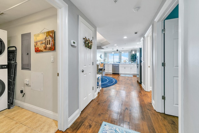 corridor featuring sink, electric panel, stacked washer and dryer, and light hardwood / wood-style floors