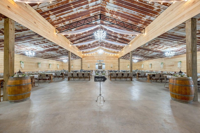 misc room with concrete flooring, high vaulted ceiling, an inviting chandelier, and wood walls