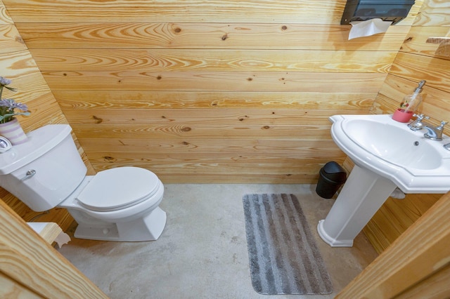 bathroom featuring toilet, wood walls, and sink