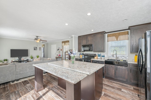 kitchen featuring dark brown cabinets, black appliances, wood-type flooring, a center island, and sink