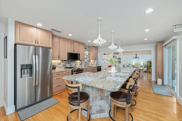 kitchen with appliances with stainless steel finishes, a kitchen island, light stone countertops, and light hardwood / wood-style floors