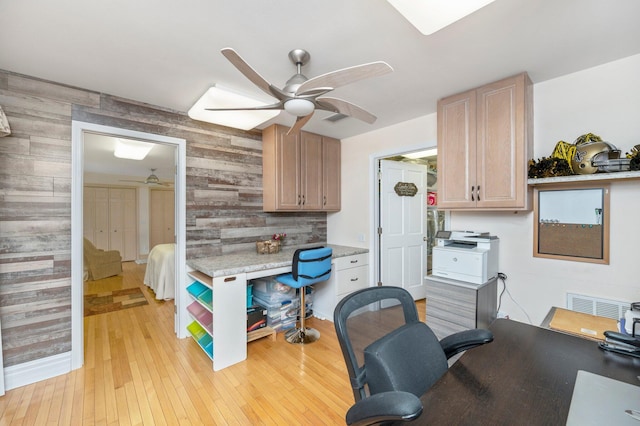 interior space with light wood-type flooring, ceiling fan, and wooden walls