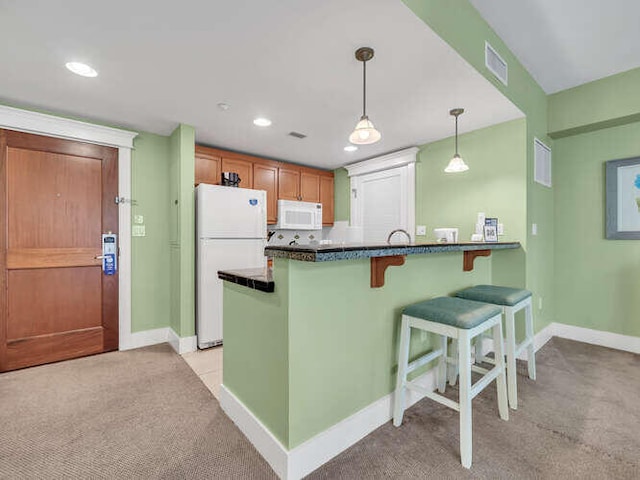 kitchen with white appliances, kitchen peninsula, light colored carpet, and decorative light fixtures