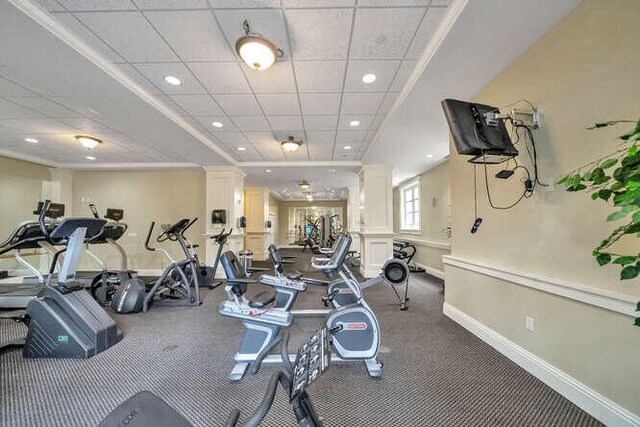 exercise room featuring ornamental molding, a paneled ceiling, and ornate columns