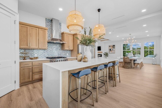 kitchen featuring hanging light fixtures, light hardwood / wood-style flooring, wall chimney range hood, a center island, and an inviting chandelier