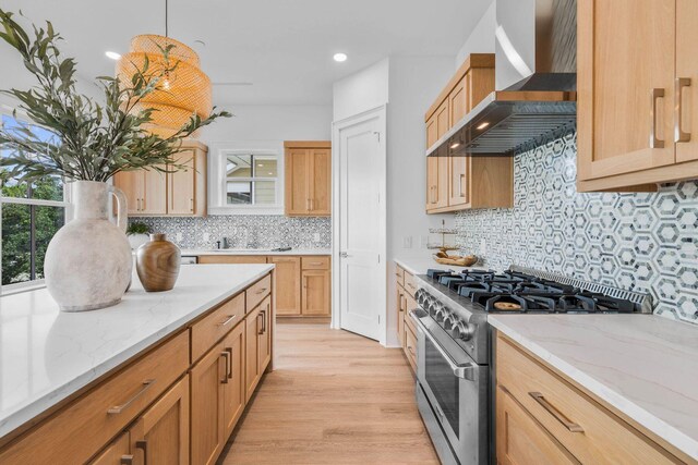 kitchen featuring light hardwood / wood-style floors, backsplash, decorative light fixtures, wall chimney range hood, and stainless steel range