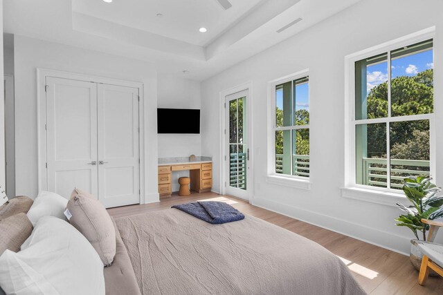 bedroom with access to outside, light wood-type flooring, and a tray ceiling