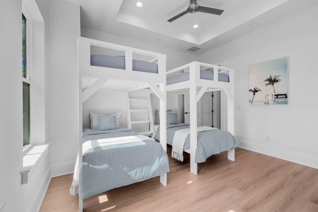 bedroom with ceiling fan, light hardwood / wood-style flooring, a raised ceiling, and multiple windows